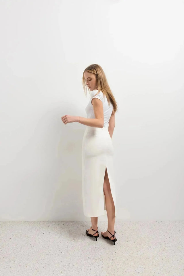 Femme de dos dans une jupe blanche longue femme, mettant en valeur la fente arrière subtile dans un cadre épuré.
