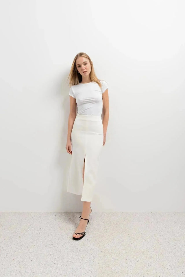 Femme posant avec une jupe blanche longue femme, accentuant la fente arrière élégante dans un style décontracté.