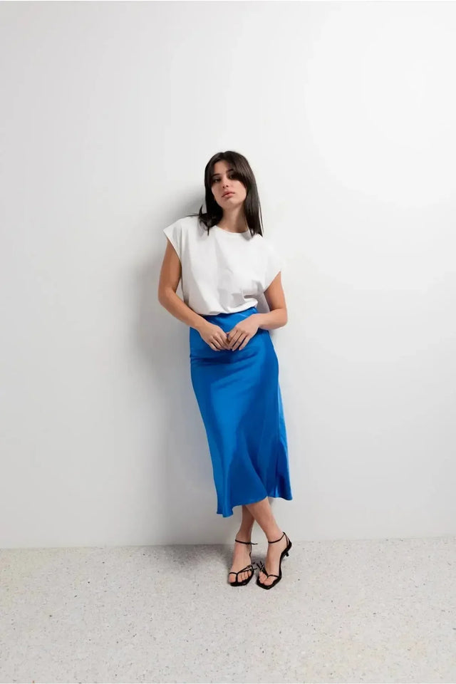 Femme portant la Jupe Satin Bleue Électrique Midi, élégante et flatteuse, associée à un haut blanc, idéale pour un look décontracté.