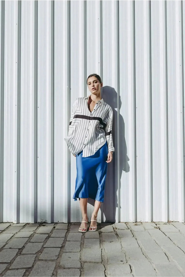 Femme dans la Jupe Satin Bleue Électrique Midi, au style tendance, portée avec une chemise rayée pour une tenue chic.