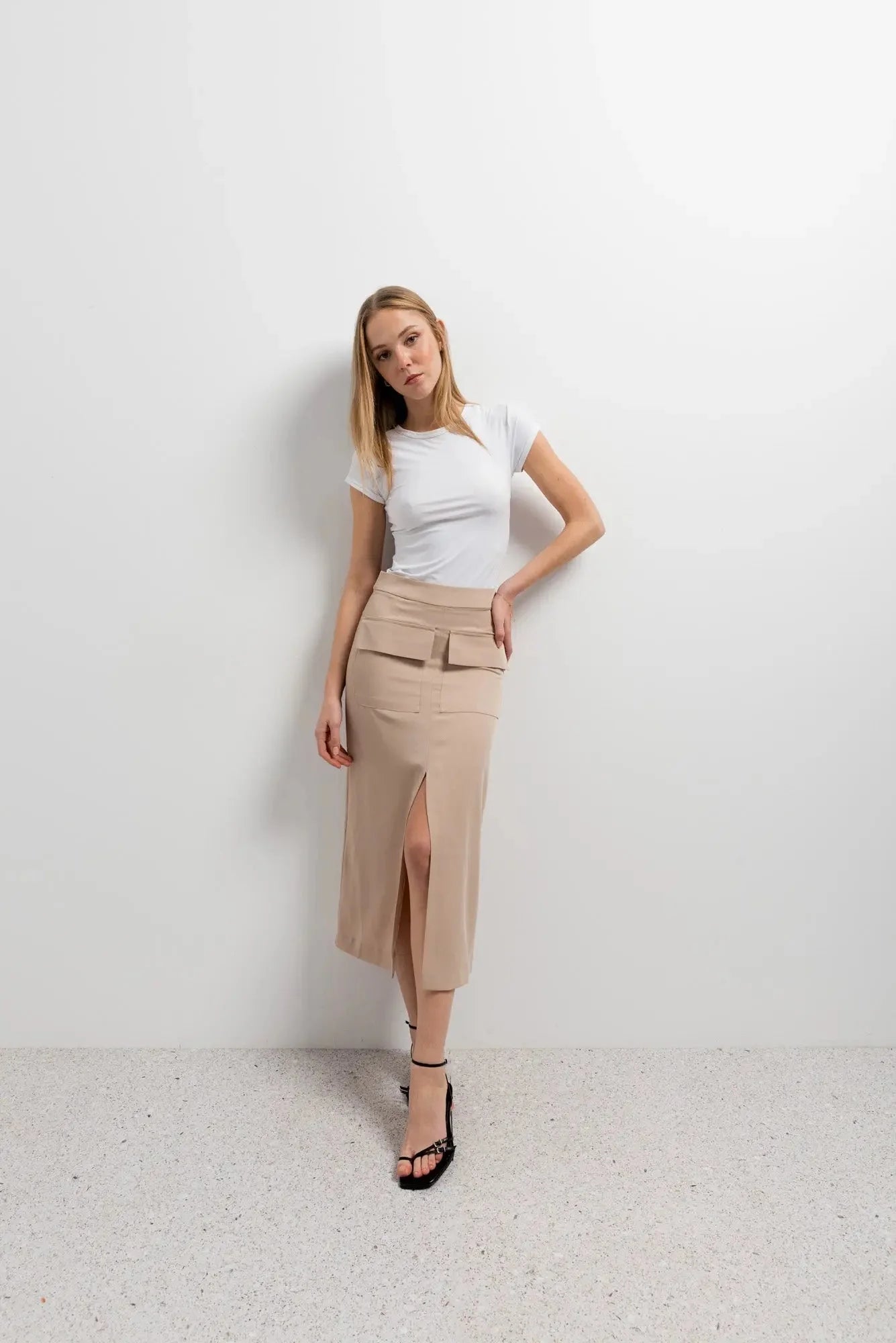 Femme souriante en jupe cargo femme beige et haut blanc, dans un décor minimaliste.