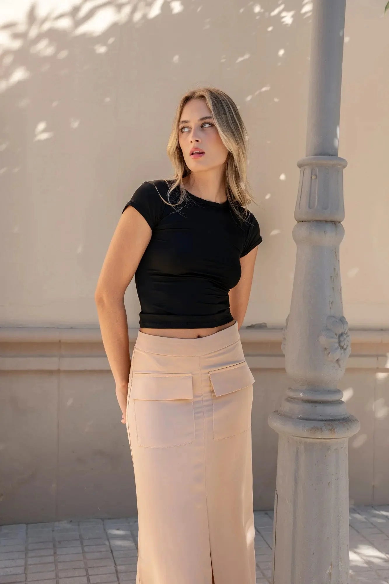 Femme stylée en jupe cargo femme beige, regardant vers le bas, avec un haut noir dans un cadre urbain.