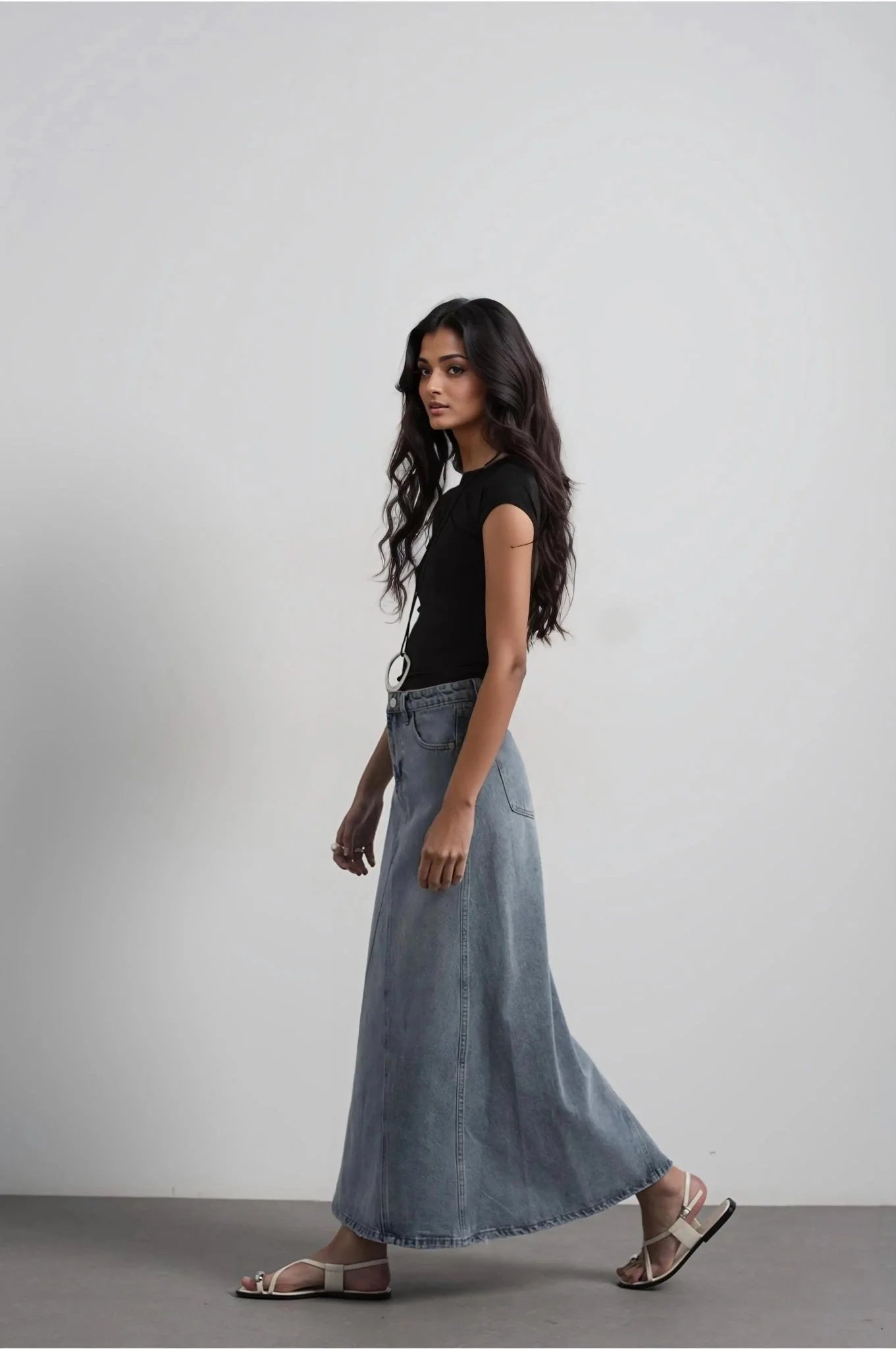 Modèle portant une jupe jean femme bleu délavé élégante et confortable, idéale pour toutes occasions, avec un t-shirt noir et des sandales.