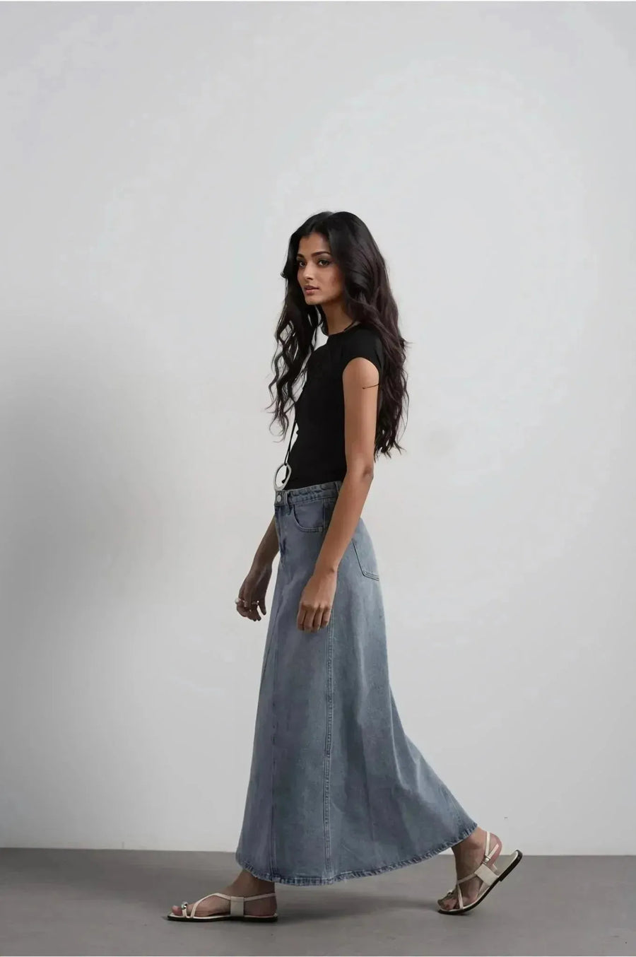 Modèle portant une jupe jean femme bleu délavé élégante et confortable, idéale pour toutes occasions, avec un t-shirt noir et des sandales.