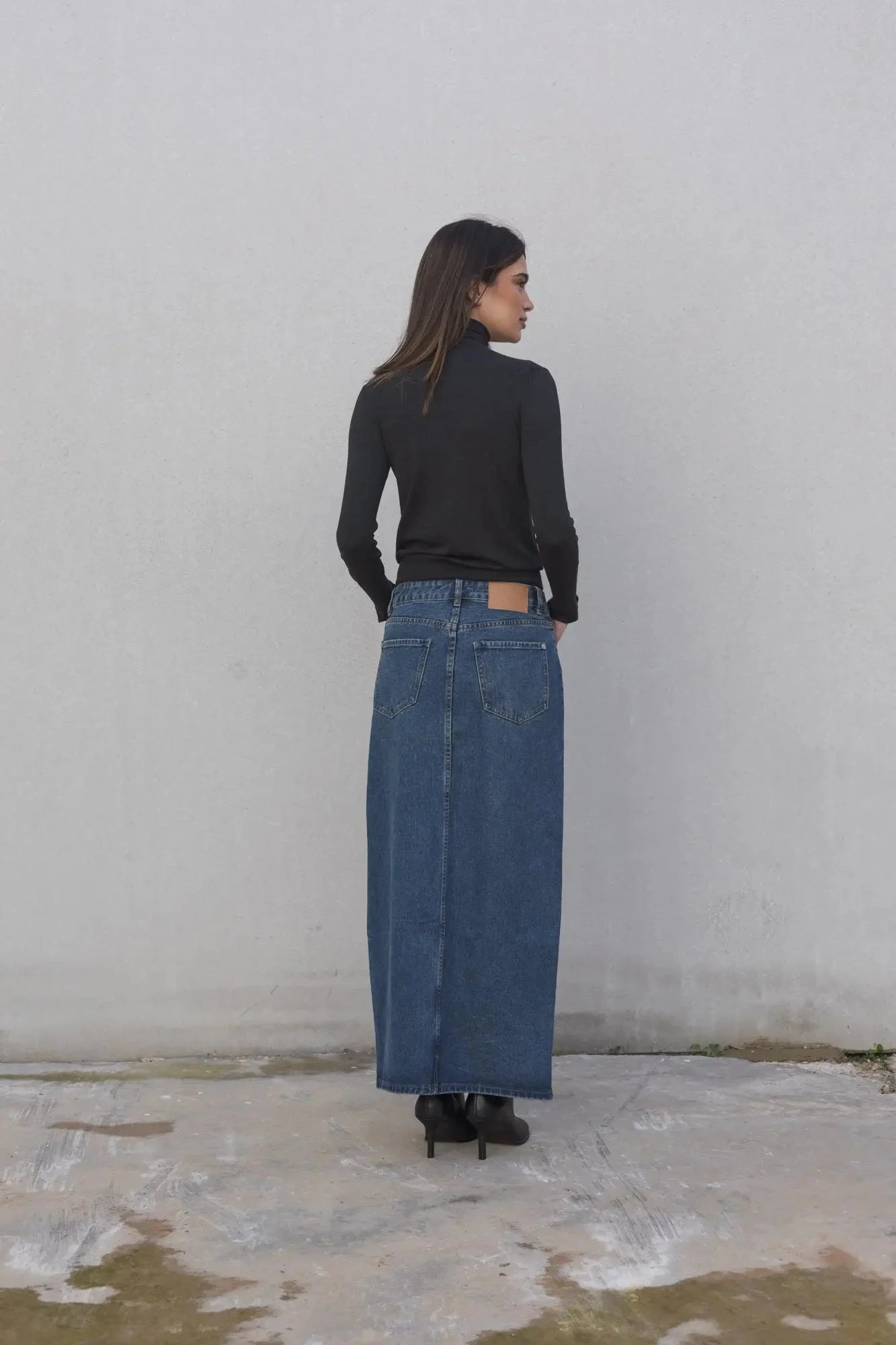 Vue arrière d'un modèle avec une jupe jean longue, soulignant le style chic et la durabilité du denim. Élégance moderne pour toutes les occasions.