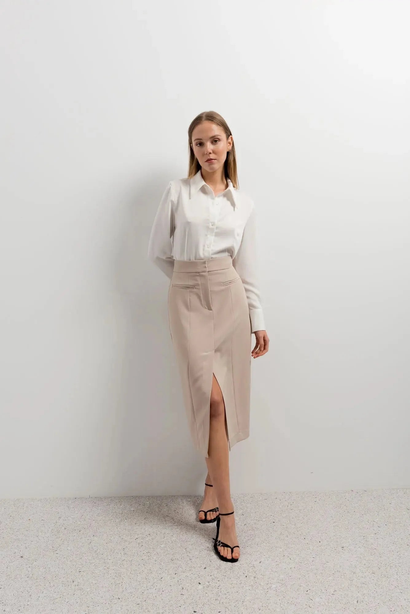 Femme portant une jupe midi fente beige, chemise blanche et sandales noires