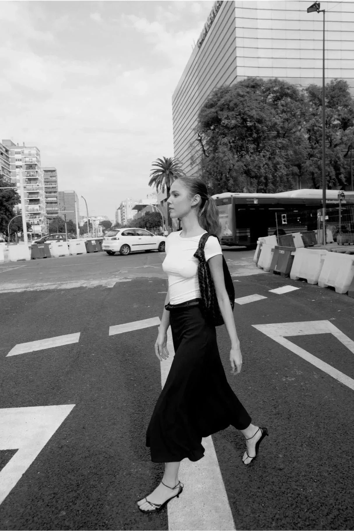 Femme marchant dans la rue en portant une jupe avec ceinture, captured in noir et blanc, mettant en avant la jupe midi pour un style urbain.