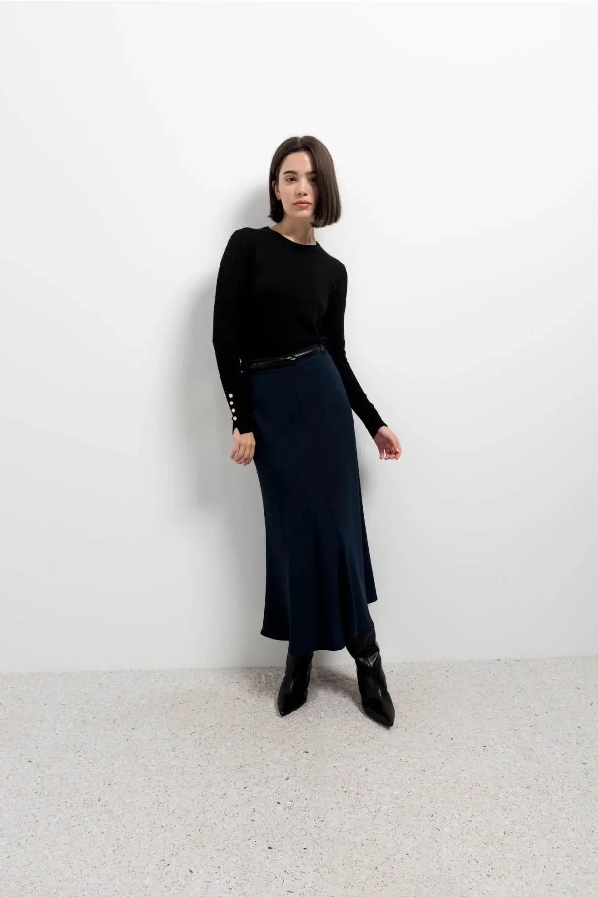 Femme portant une jupe midi navy avec ceinture, top noir et bottines noires
