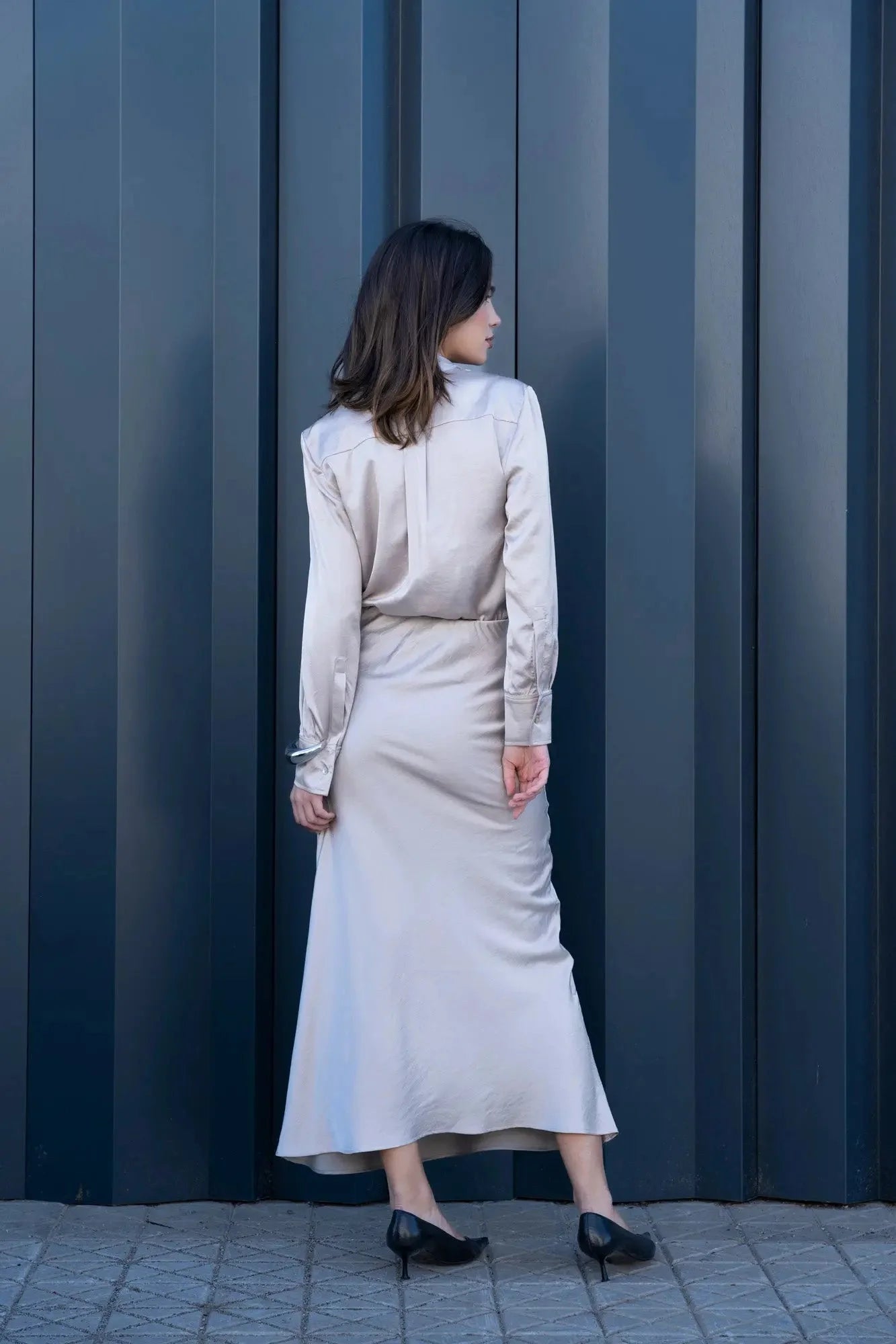 Femme portant une jupe midi en satin champagne avec chemise assortie et talons noirs