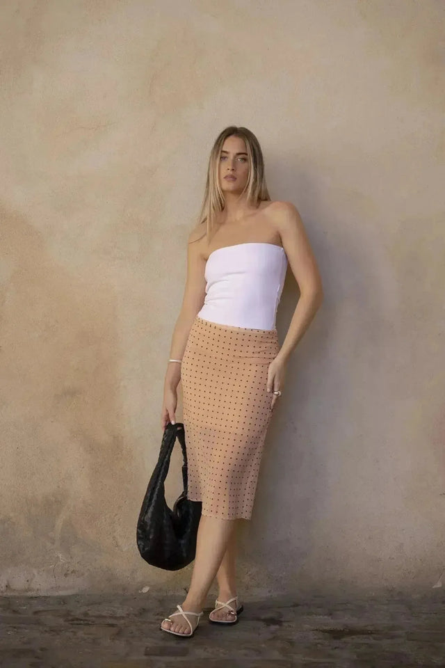 Femme portant une jupe midi imprimée à pois peach et un sac noir