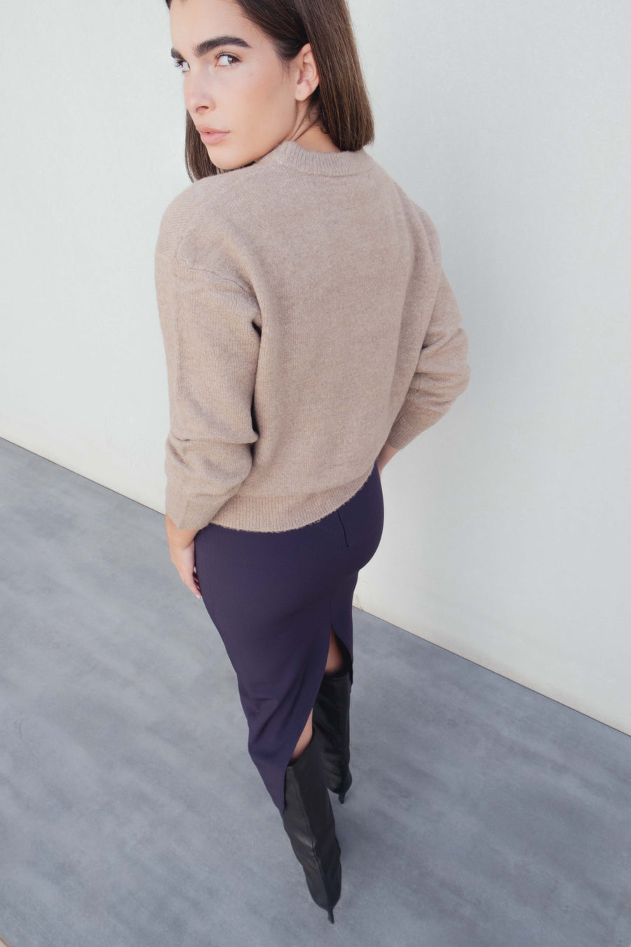 Vue arrière d'un modèle en jupe midi marine taille haute, associée à un pull beige, soulignant la coupe élégante de la jupe midi.