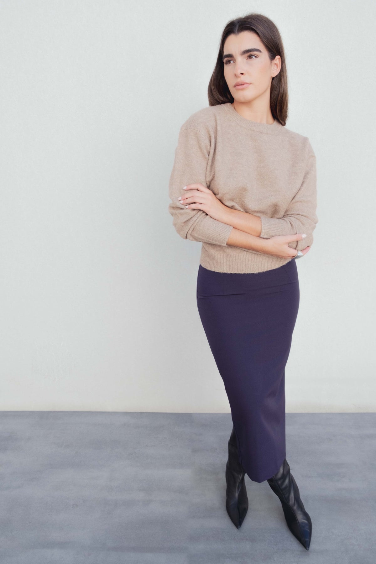 Modèle portant une jupe midi marine taille haute avec un pull beige, mettant en valeur la jupe midi dans un cadre moderne.