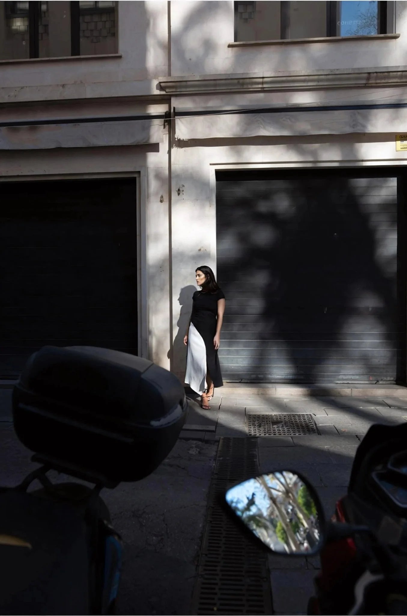 Jupe Midi Noir et Blanc Élégante et Confortable - Femme à la mode se tenant près d'un bâtiment, portant une jupe midi noir et blanc, idéale pour des occasions décontractées.