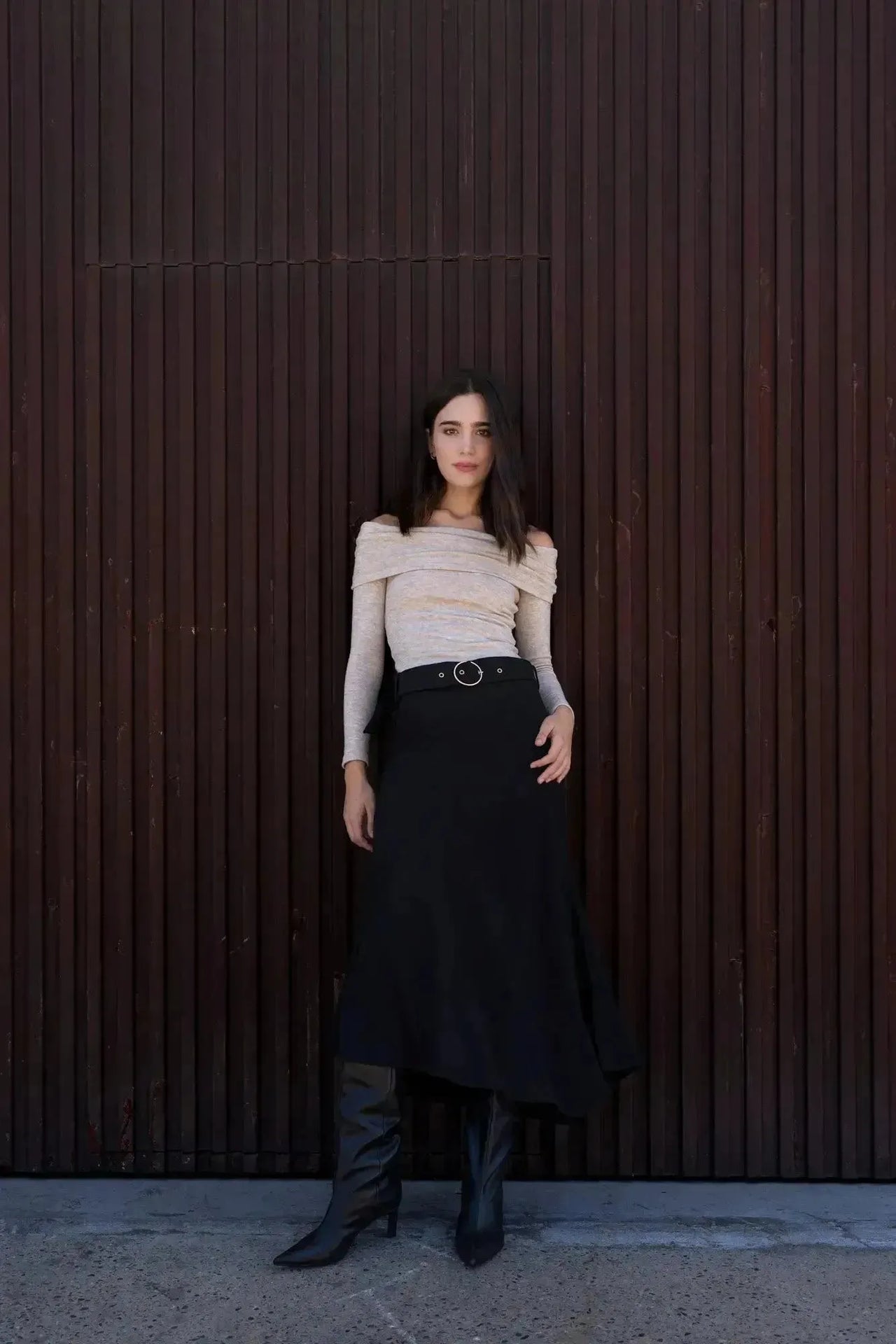 Femme portant la Jupe Midi Noire Avec Ceinture, affichant une silhouette flatteuse avec des bottes noires, parfaite pour une sortie élégante.