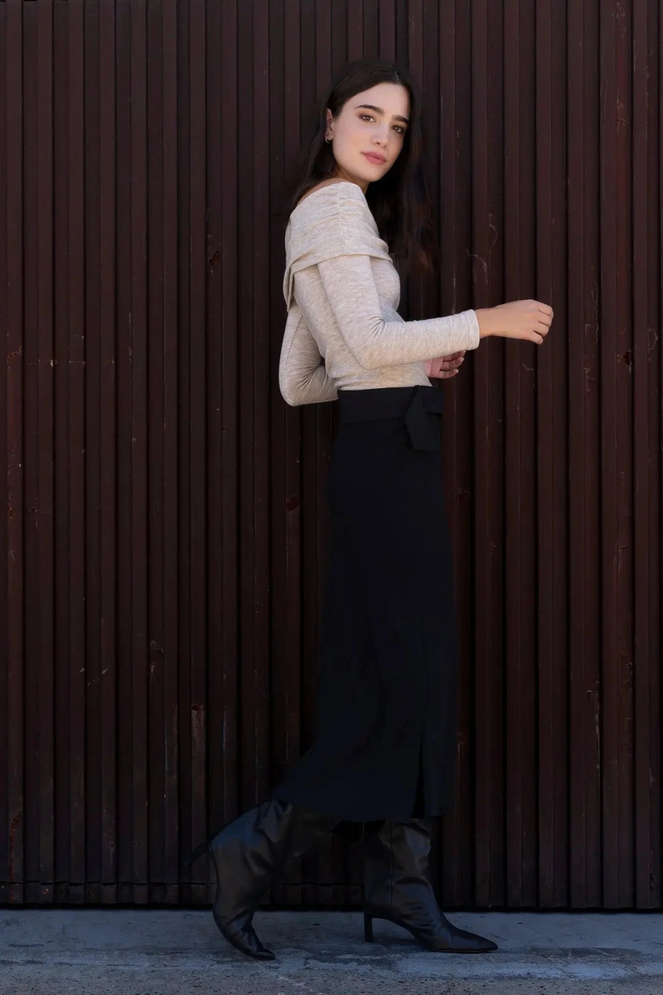 Femme portant une jupe midi noire avec ceinture, haut off-shoulder et bottes hautes