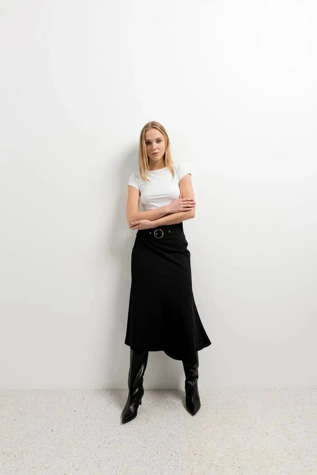 Femme posant dans la Jupe Midi Noire Avec Ceinture, avec un style minimaliste et des bottes raffinées, idéale pour une tenue de bureau.