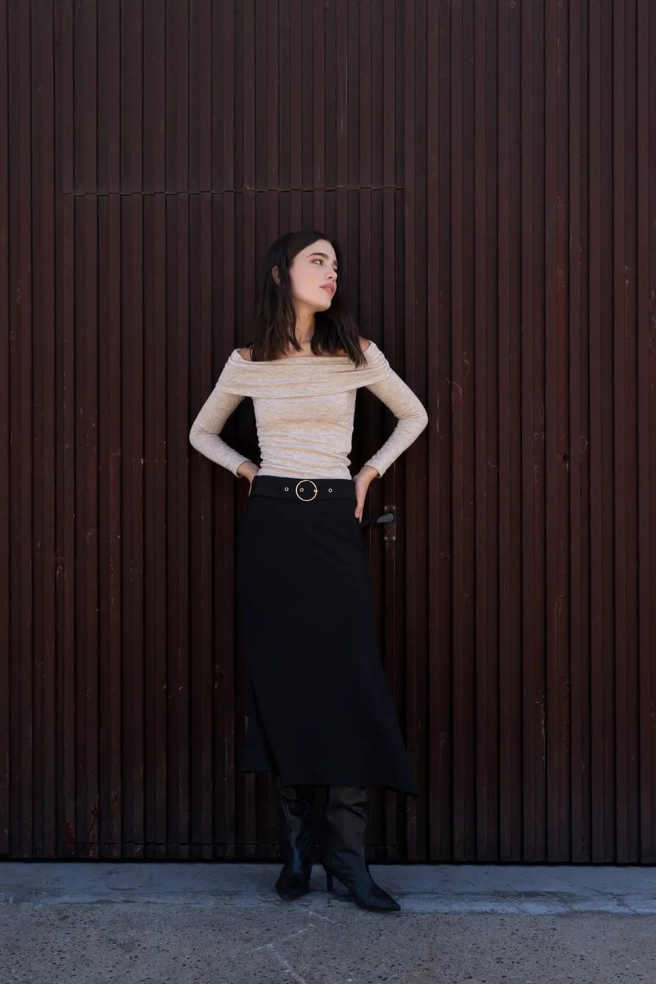 Femme portant une jupe midi noire avec ceinture, top épaules dénudées et bottines noires