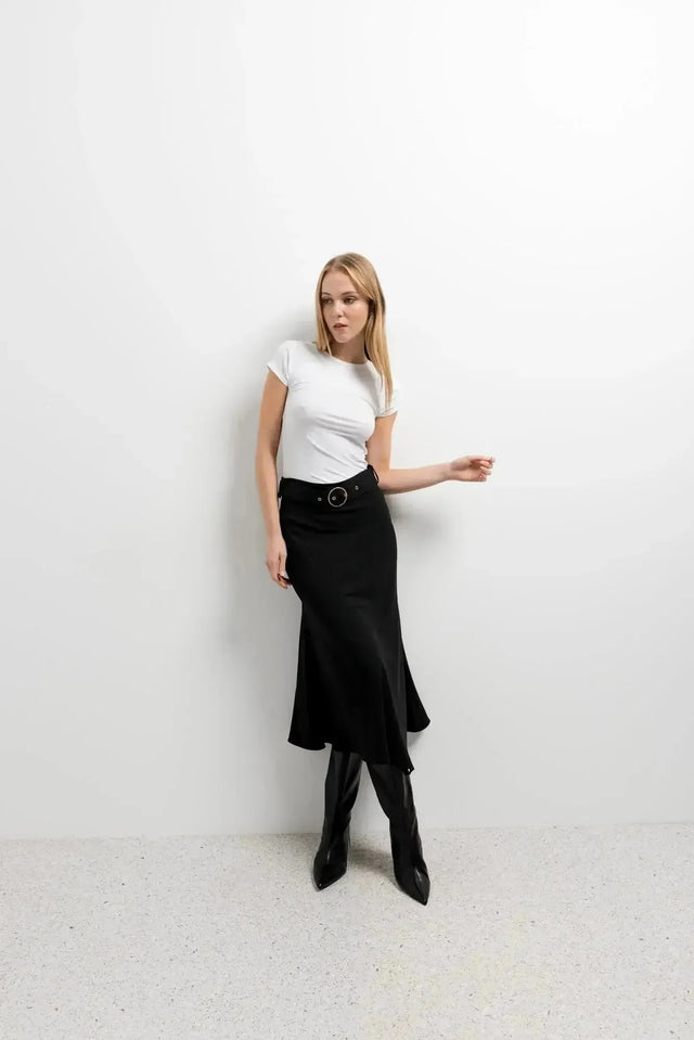 Femme dans la Jupe Midi Noire Avec Ceinture, adoptant un look moderne avec un haut ajusté et des bottes, parfait pour un style quotidien.