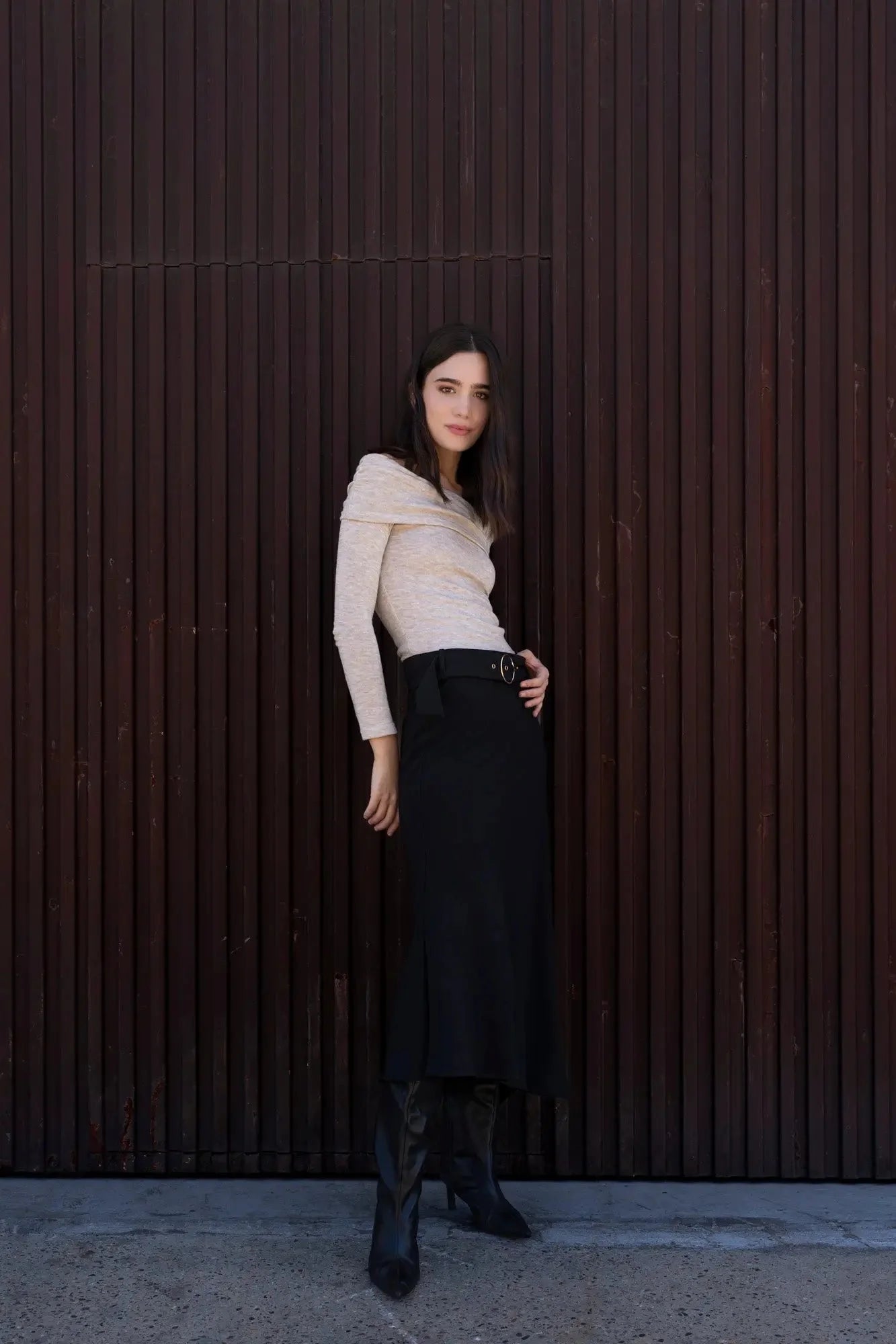 Femme portant une jupe midi noire avec ceinture, top beige et bottines noires