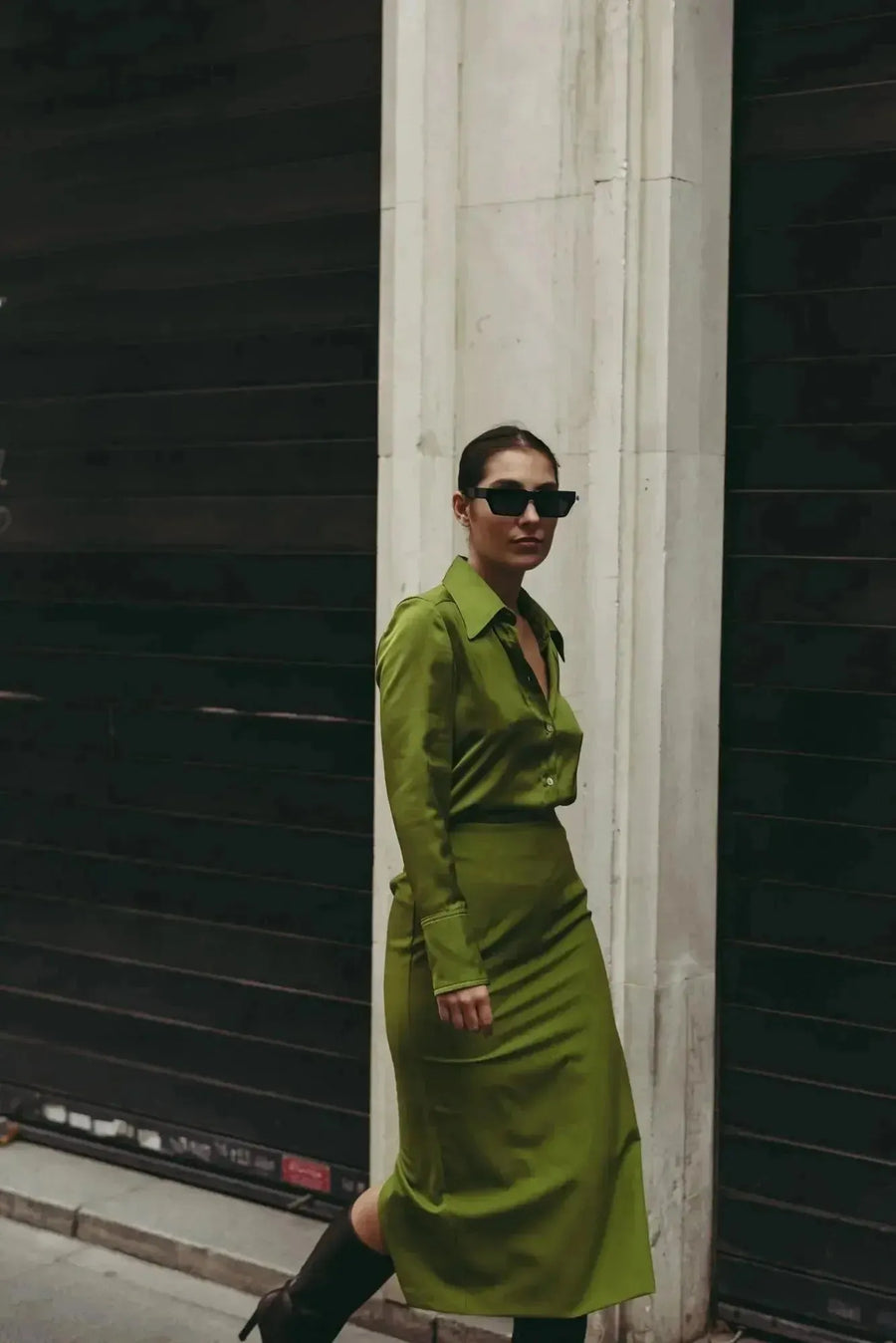 Femme marchant dans une jupe verte satin longue et chic, avec une fente latérale, offrant un look polychrome moderne, parfait pour diverses occasions.