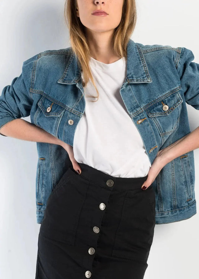 Close-up sur une femme portant une jupe bouton devant noire en denim, avec une veste en jean, affichant un style casual et élégant.
