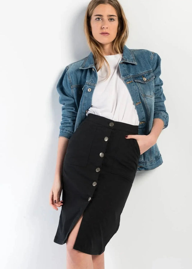 Femme stylée avec une jupe bouton devant noire en denim, associée à une veste en jean, idéale pour un look décontracté chic.