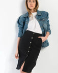 Femme stylée avec une jupe bouton devant noire en denim, associée à une veste en jean, idéale pour un look décontracté chic.