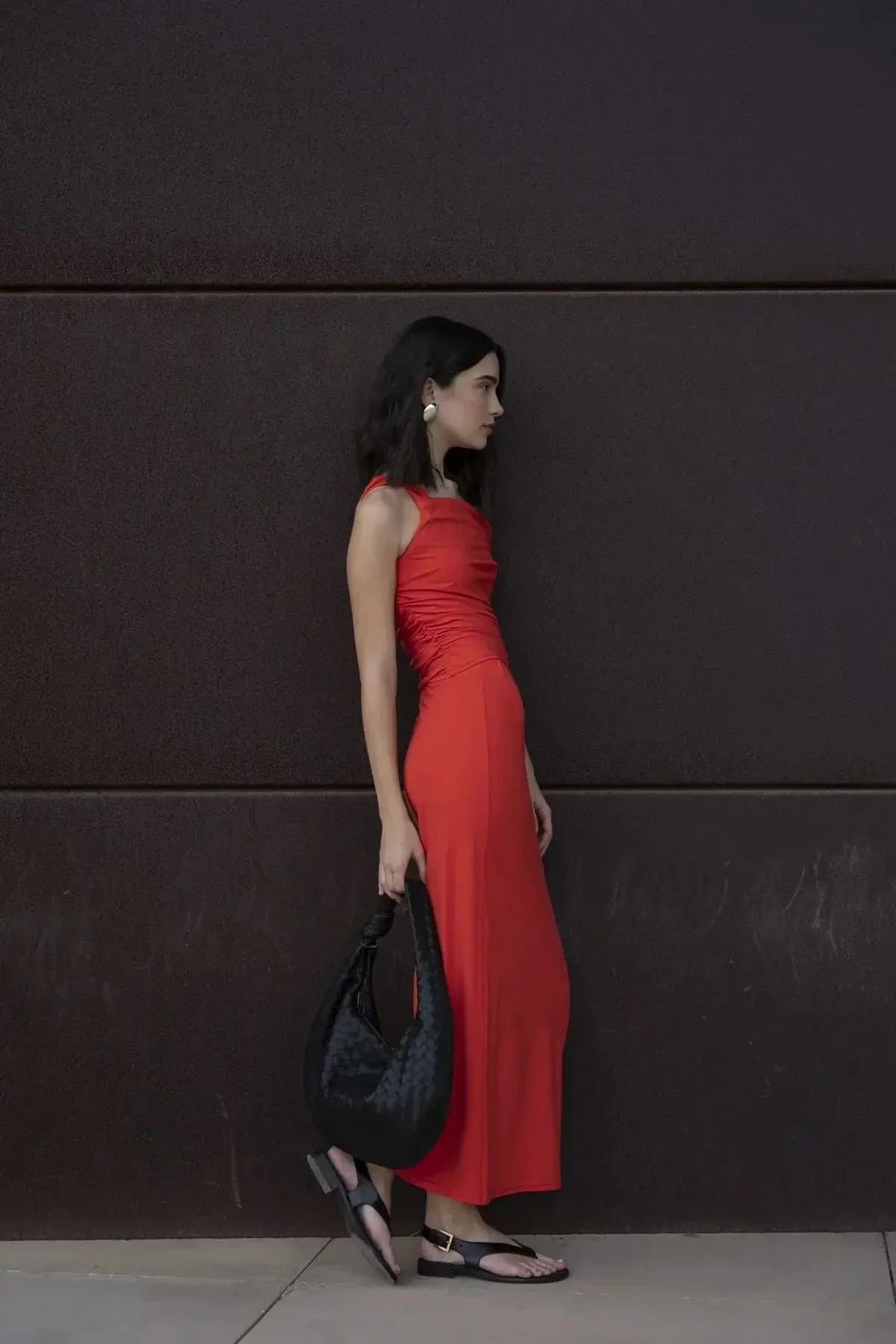 Modèle stylé avec une jupe rouge longue moulante taille basse en polyamide, en pose sur un fond urbain, mettant en avant un look moderne.