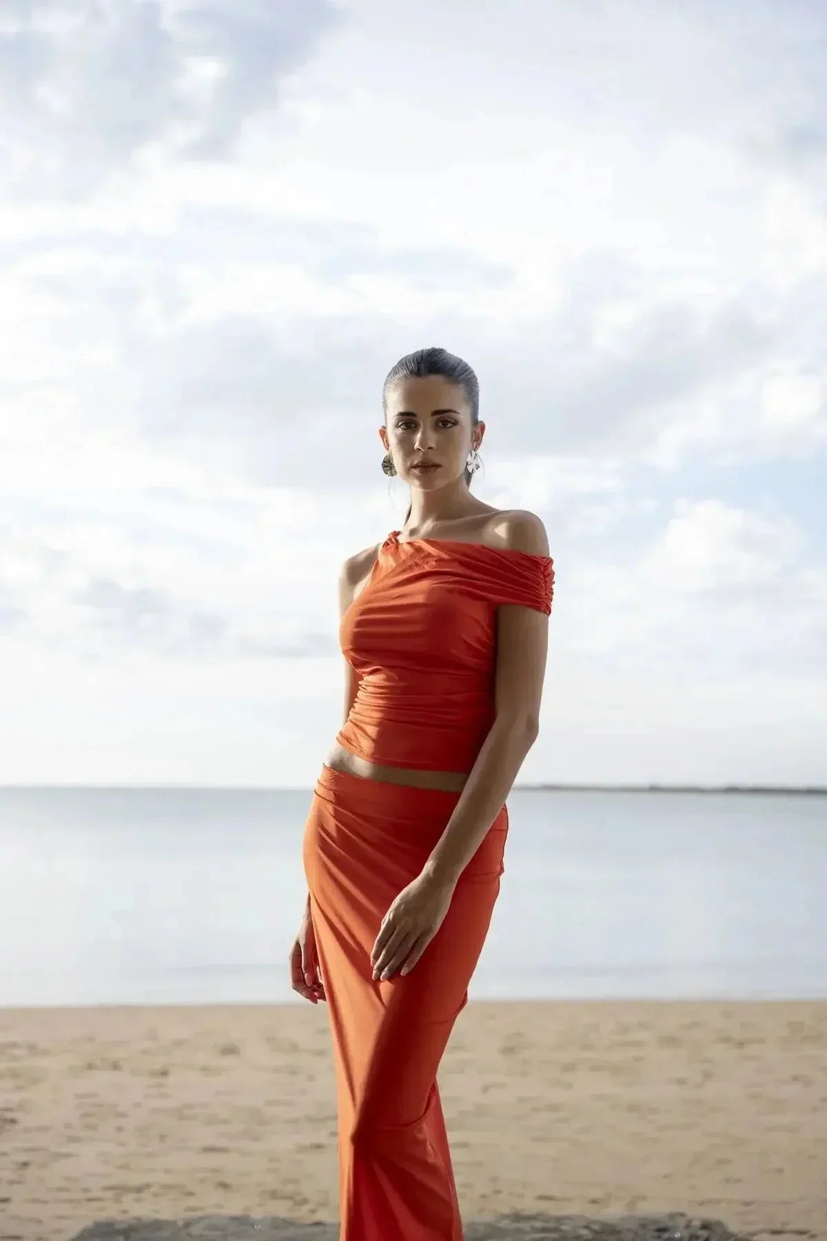 Femme en jupe rouge longue moulante taille basse en polyamide sur la plage, affichant un look moderne et sensuel avec fente.