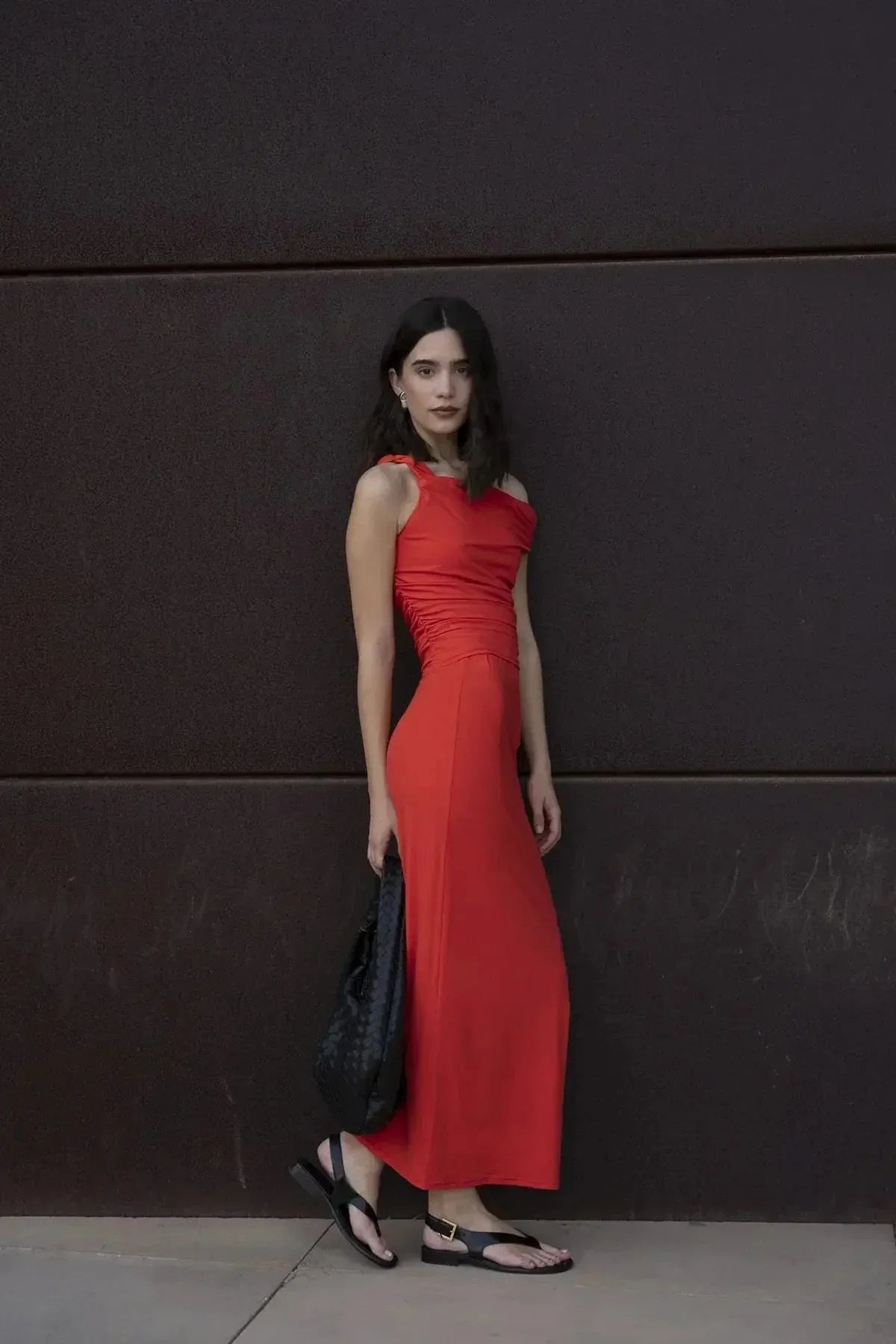 Modèle portant une jupe rouge longue moulante taille basse en polyamide, style chic avec drapé élégant, posé devant un mur.