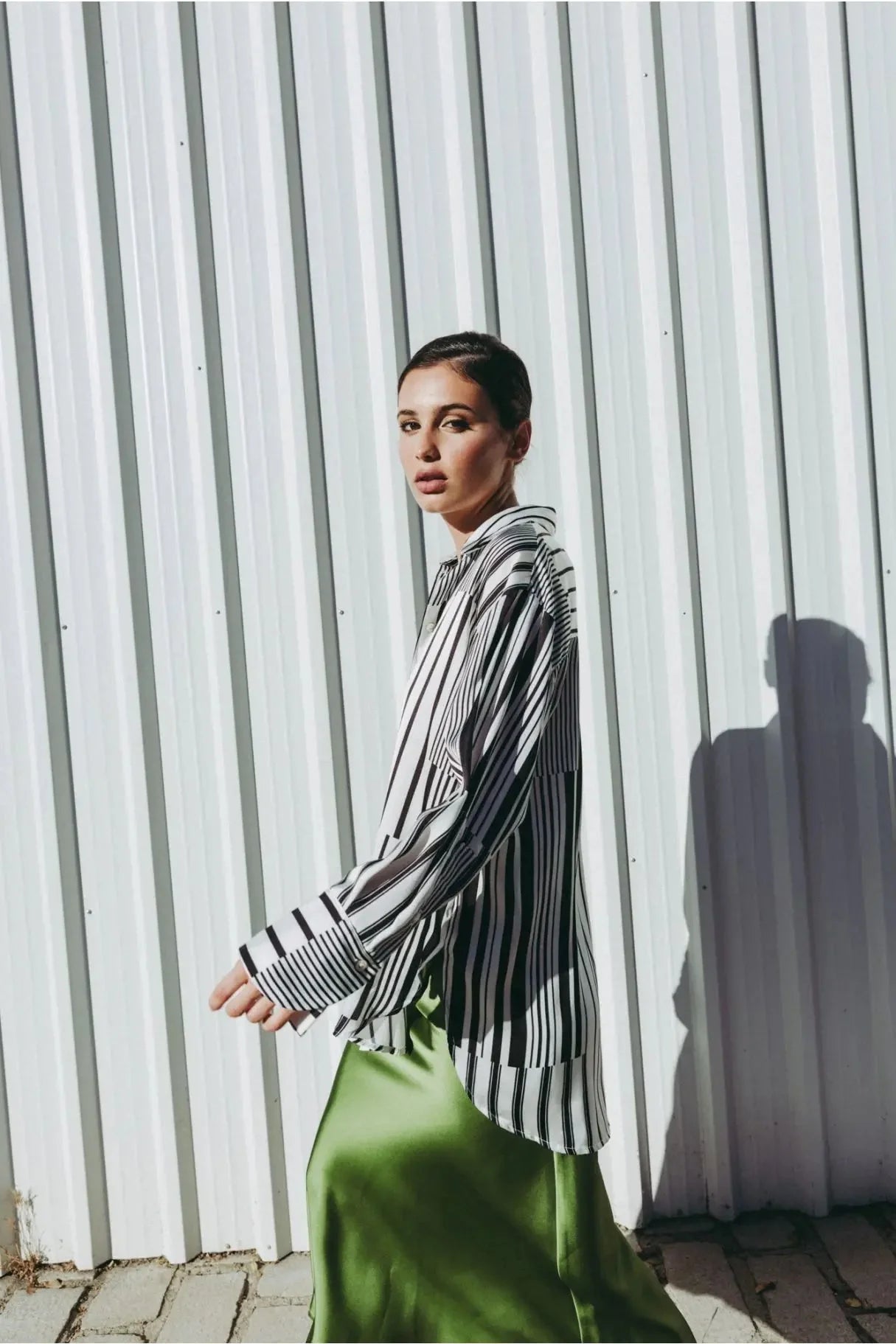 Femme se déplaçant avec style en jupe verte satin et chemise à rayures, capturant l'essence de la mode contemporaine.
