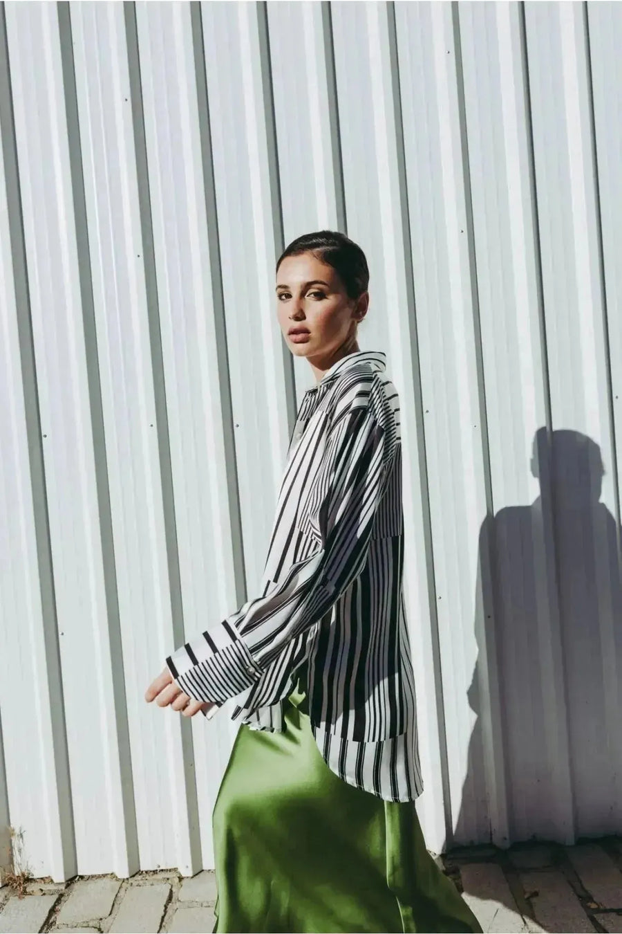 Femme se déplaçant avec style en jupe verte satin et chemise à rayures, capturant l'essence de la mode contemporaine.