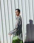 Femme se déplaçant avec style en jupe verte satin et chemise à rayures, capturant l'essence de la mode contemporaine.