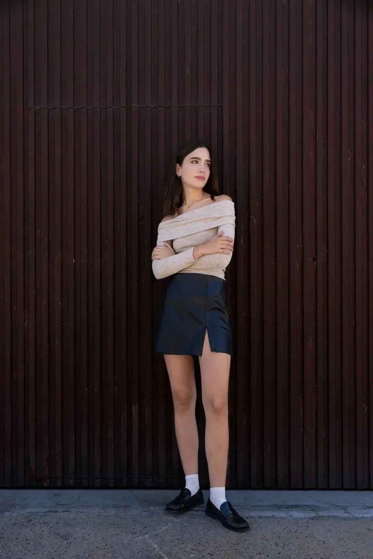 Femme élégante avec une jupe short simili cuir noir fendue, croisant les bras devant un mur, démontrant le style moderne de cette pièce.