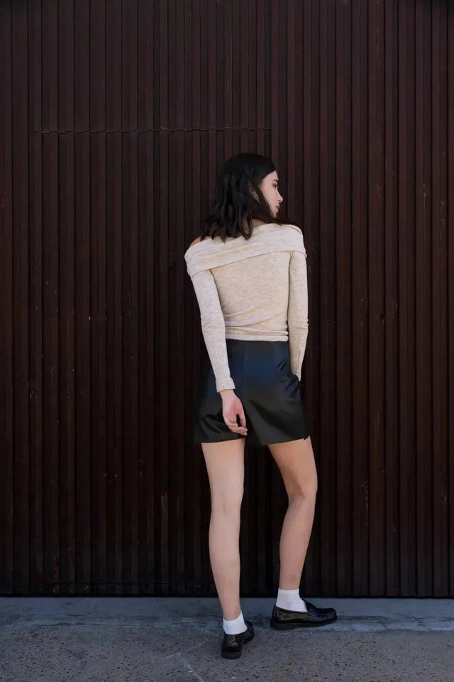 Vue arrière d'une femme en jupe short simili cuir noir fendue, montrant la coupe élégante et tendance de cette pièce pour femmes.