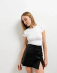 Femme en jupe short simili cuir noir fendue, penchée en avant, illustrant le confort et la modernité de cette pièce pour femmes.