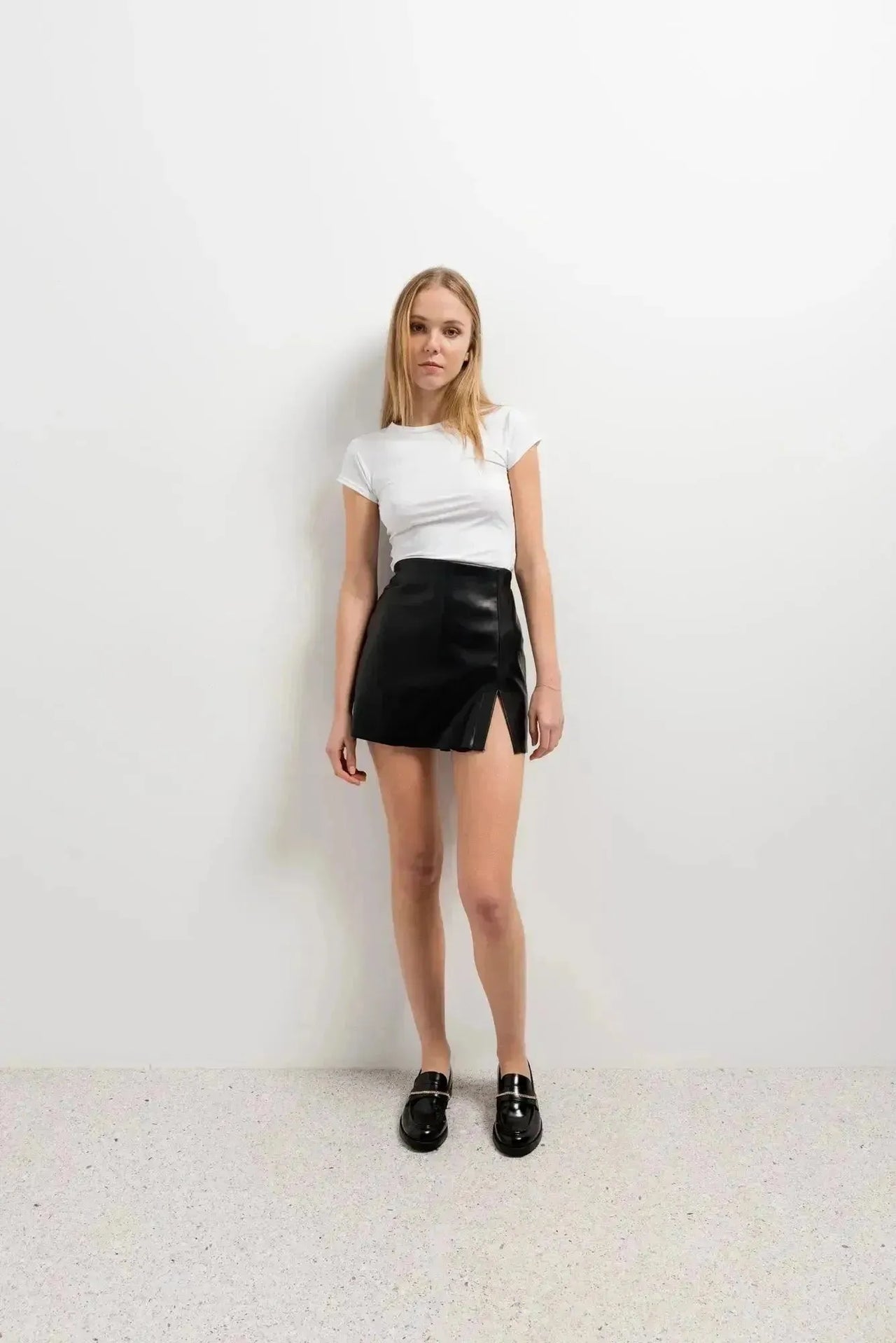Modèle portant une jupe short simili cuir noir fendue, avec un t-shirt blanc, mettant en avant un style décontracté et élégant.