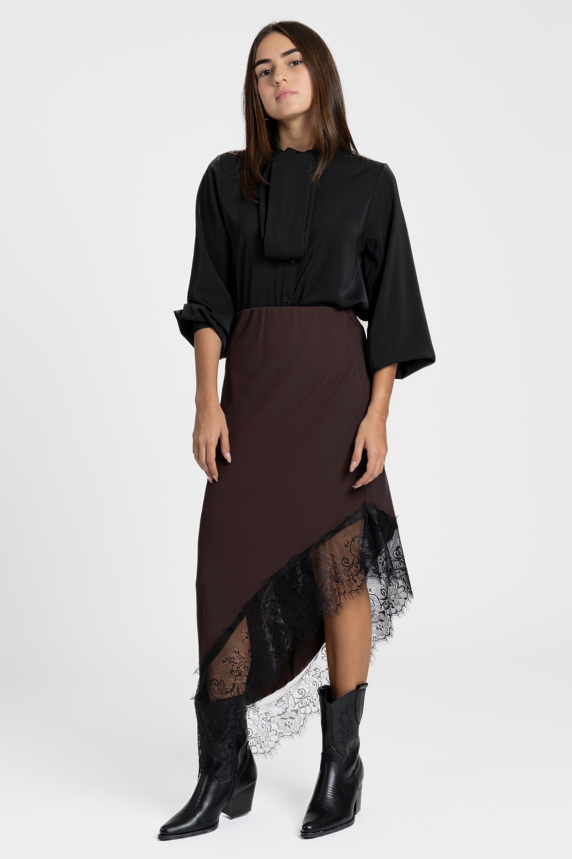 Modèle féminin en jupe dentelle asymétrique marron, ajoutant une touche élégante à sa tenue.