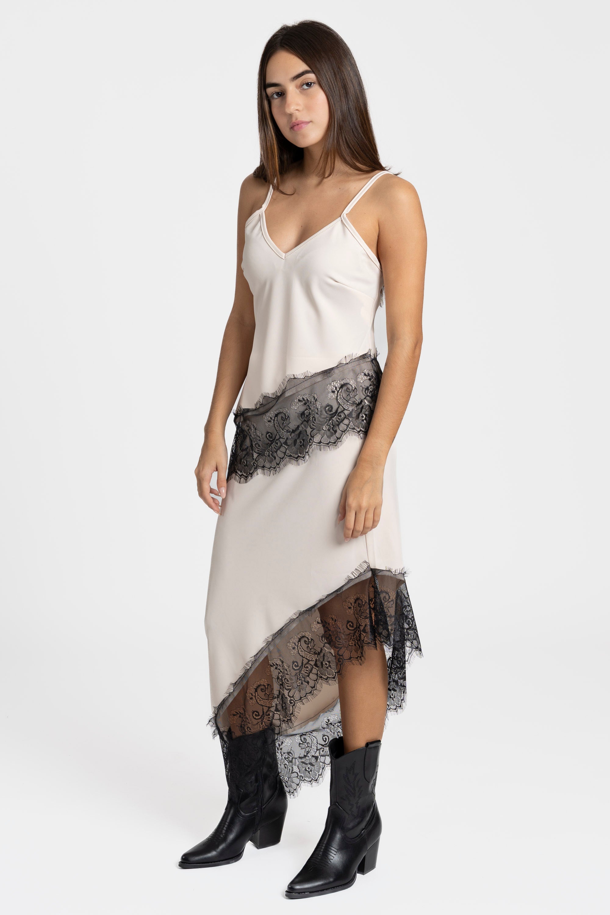 Modèle féminin posant avec confiance dans une jupe dentelle asymétrique beige, associée à des bottes noires.