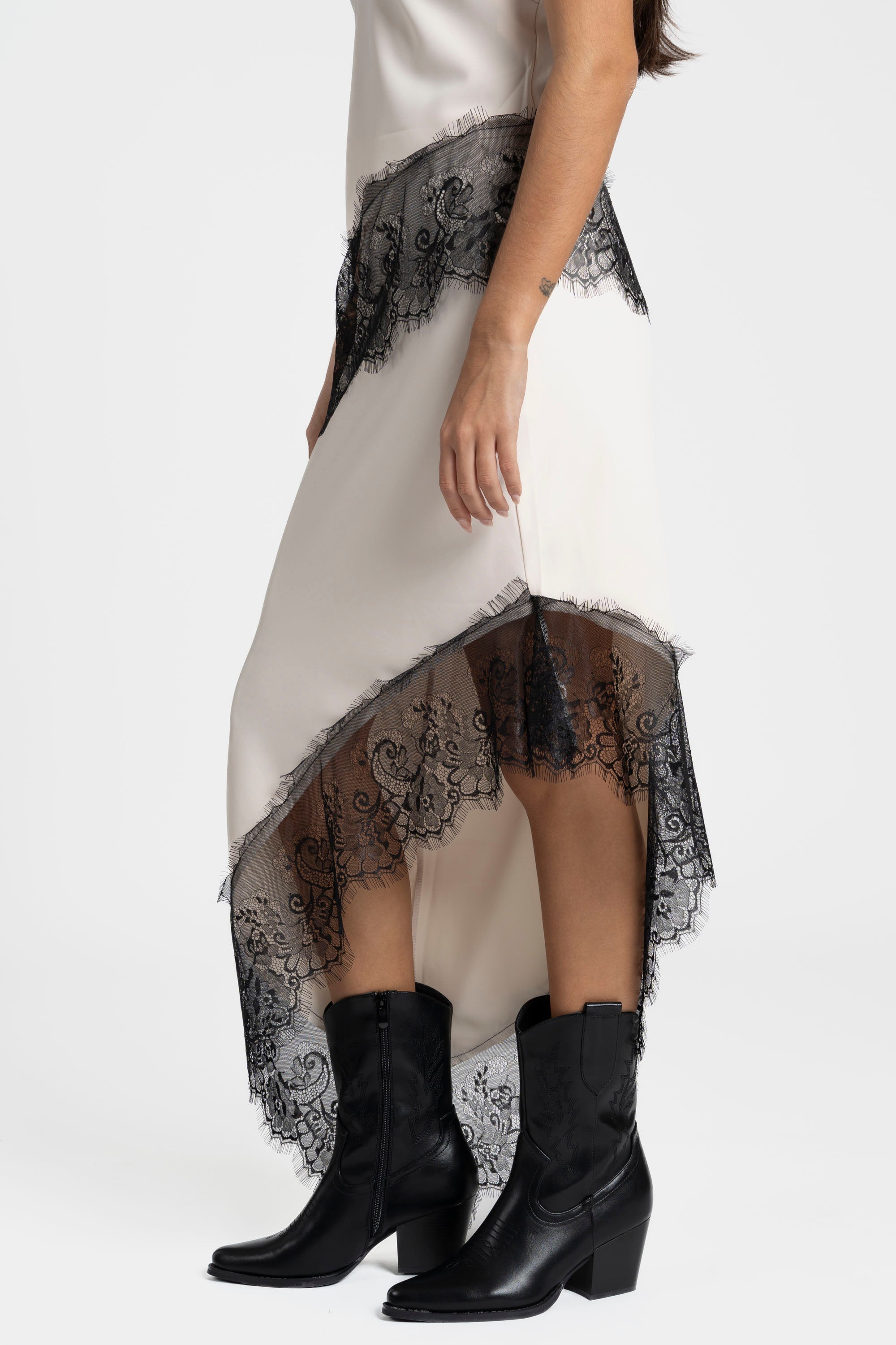 Détail de la jupe dentelle asymétrique beige mettant en évidence l'ourlet en dentelle noire, idéale pour les événements chic.