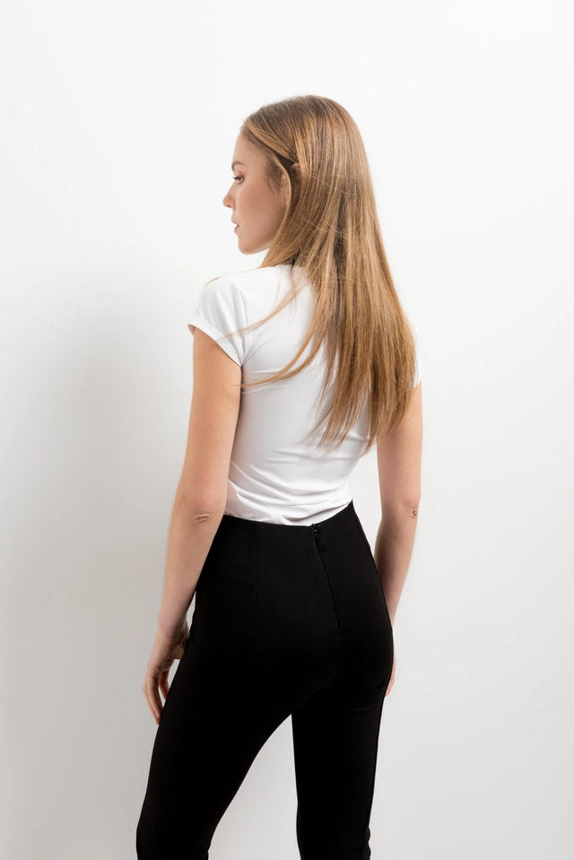 Vue arrière de femme en haut blanc et leggings évasé noir à fentes, soulignant le style moderne.