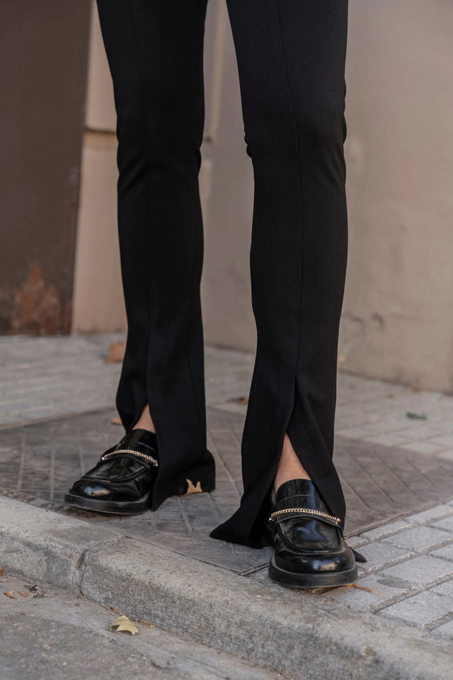Détail sur les jambes d'une femme en leggings évasé noir à fentes, montrant les chaussures et la coupe évasée.