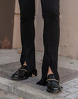 Détail sur les jambes d'une femme en leggings évasé noir à fentes, montrant les chaussures et la coupe évasée.