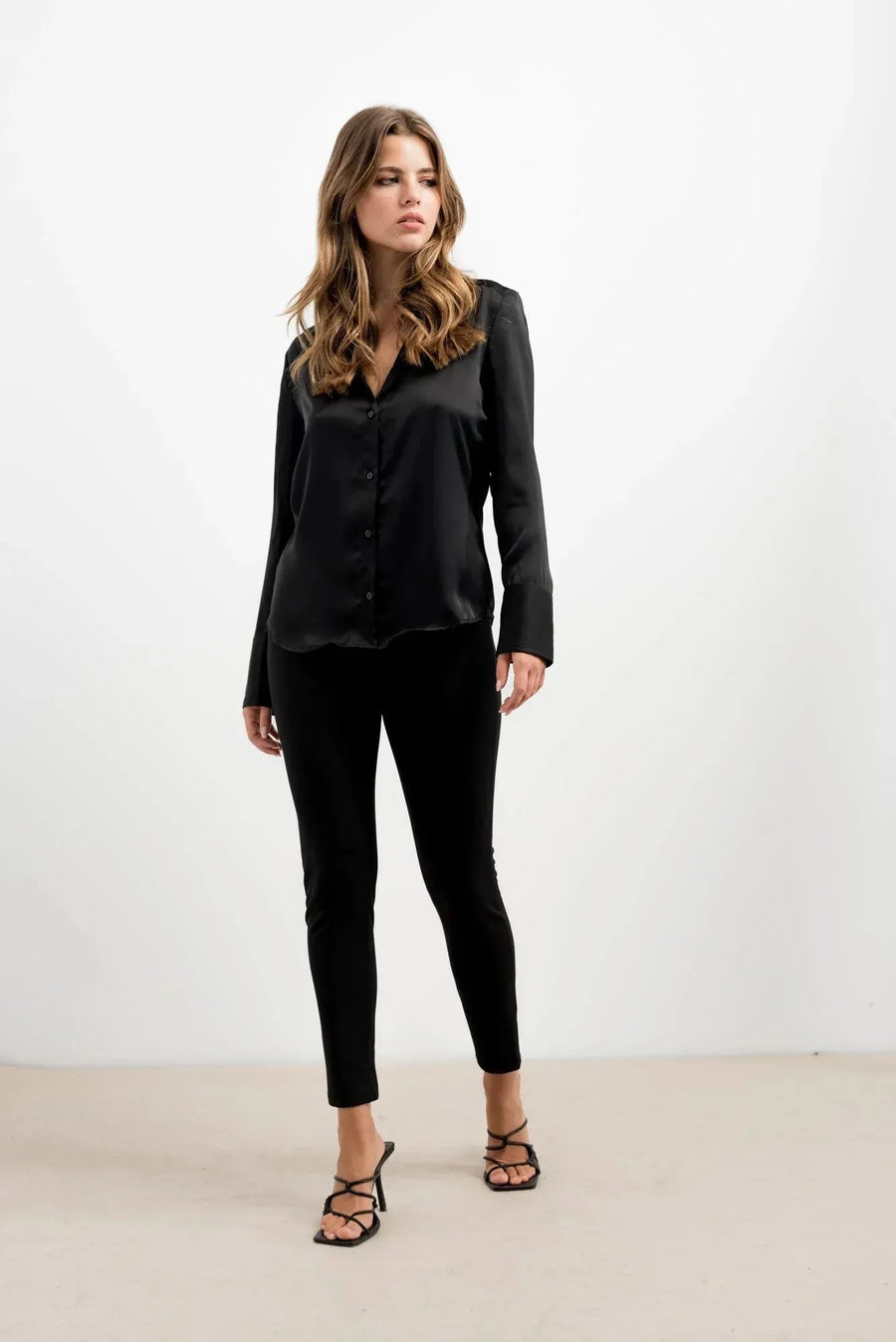 Femme portant leggings noir effet néoprène avec haut en satin noir et sandales à talons