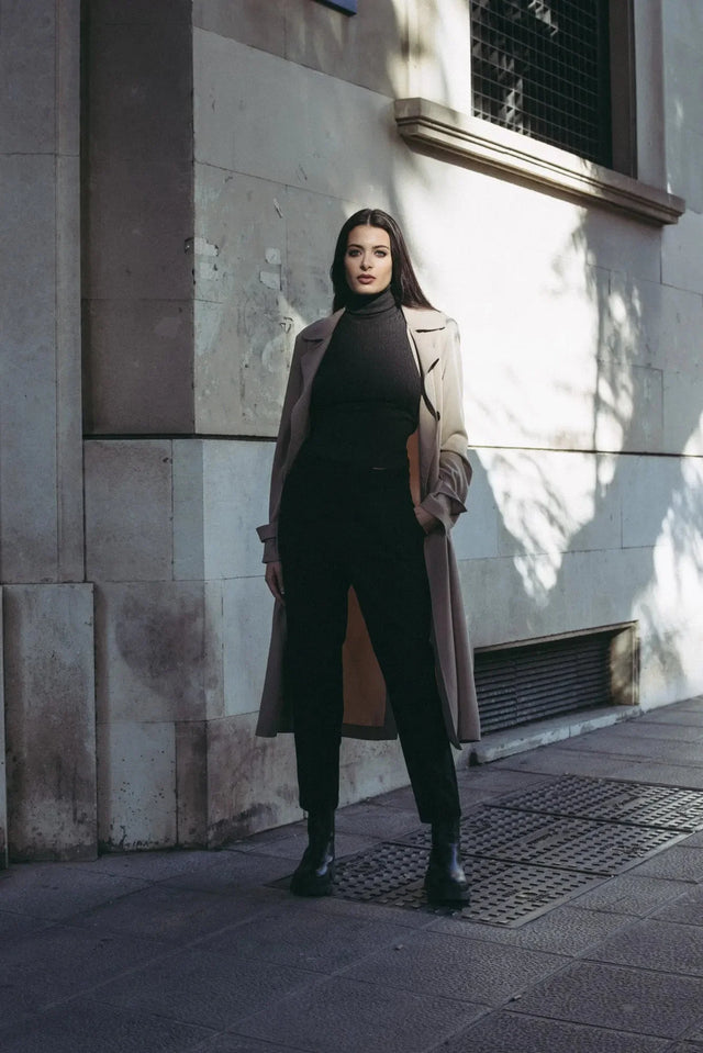 Femme élégante en pull col roulé femme sous un trench beige, une tenue idéale faisant partie des indispensables de la garde-robe d’hiver.