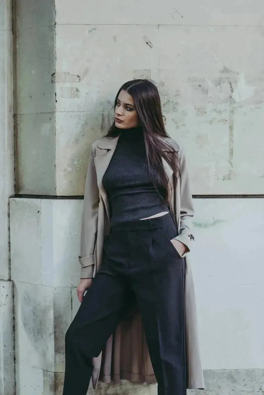 Modèle en pull col roulé femme noir, accompagné d'un trench, illustrant les indispensables de la garde-robe d’hiver.