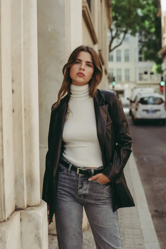 Femme avec pull col roulé femme et blazer, se promenant dans la ville, reflétant les indispensables de la garde-robe d’hiver.