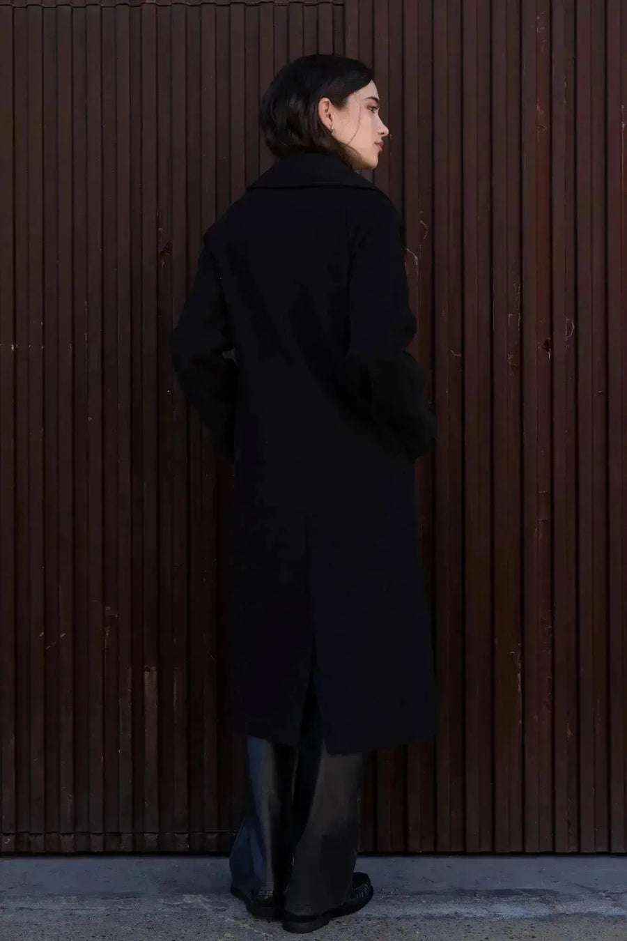 Femme de dos dans un manteau long chaud femme noir à double boutonnage, affichant une silhouette élégante.