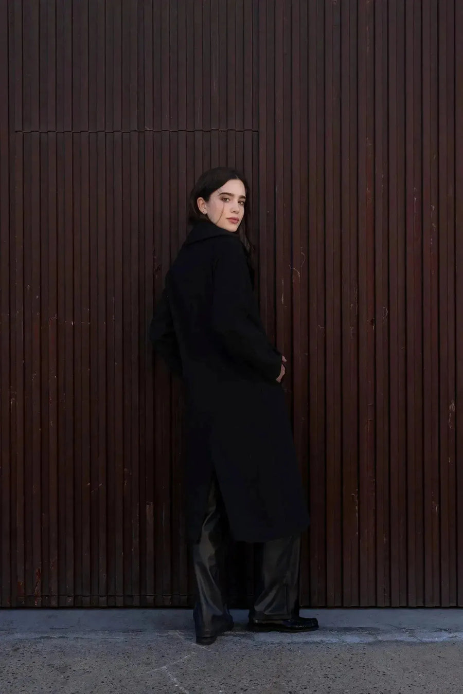 Femme montrant un manteau long chaud femme noir à double boutonnage de dos, avec un style moderne et élégant.