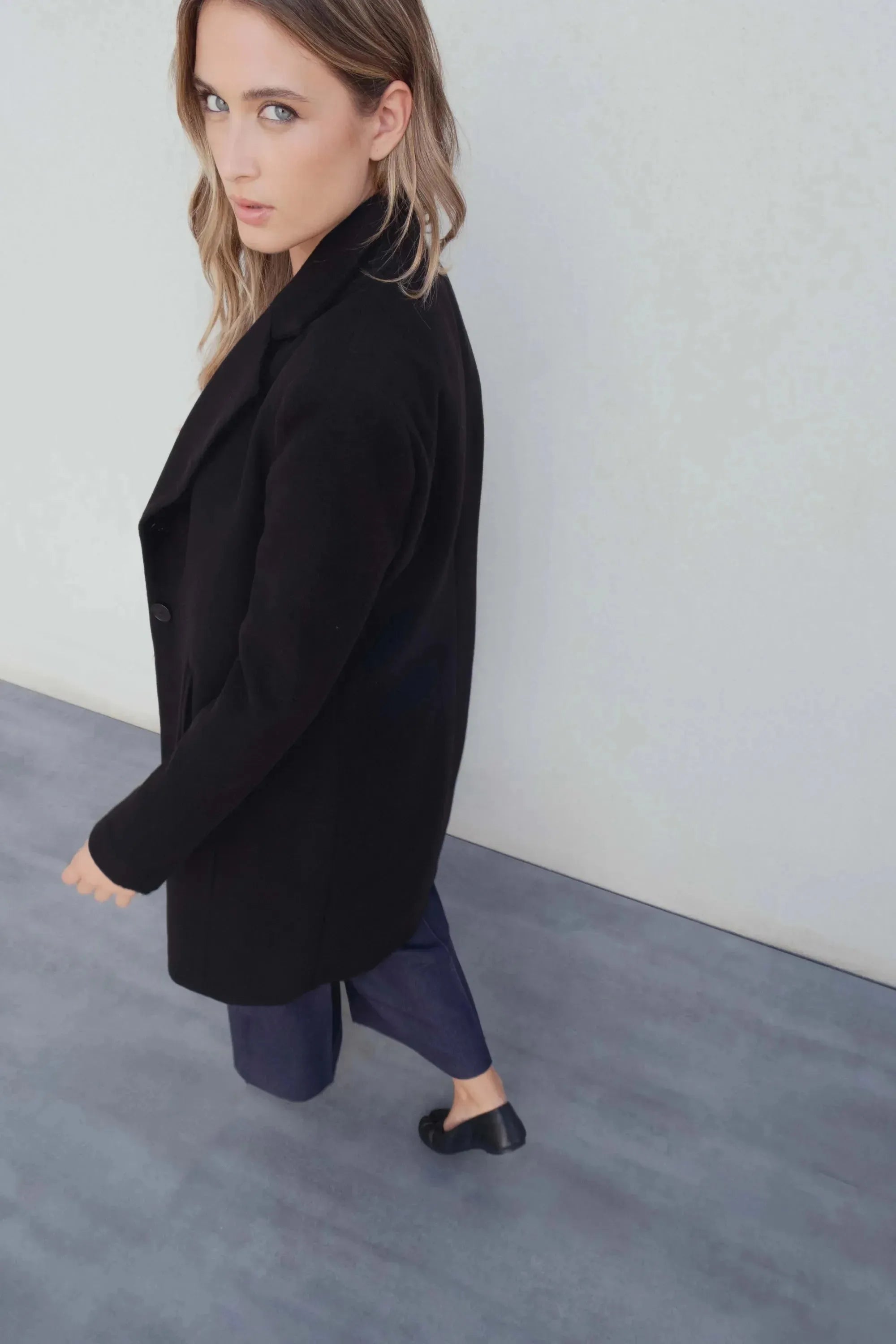 Femme portant un manteau col en noir avec blazer et pantalons bleus foncés